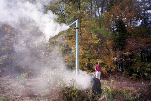 against autumn tree-lined trail, a tall metal release valve billows own steam startling a pedestrian in purple shirt