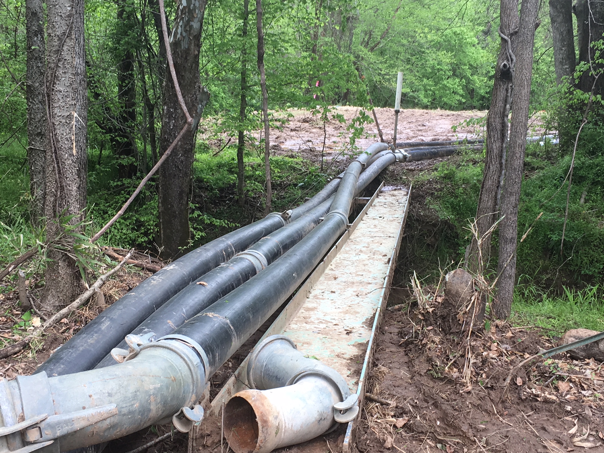3 large rubber pipelines run past a tree line divert water down towards a raging muddy creek