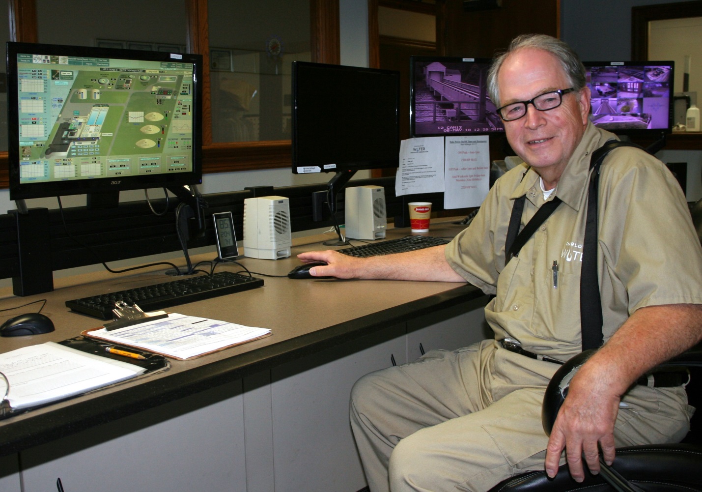 utility engineer in tan shirt and pants sits at desk smiling as he reviews status of the water treatment plant on his screen