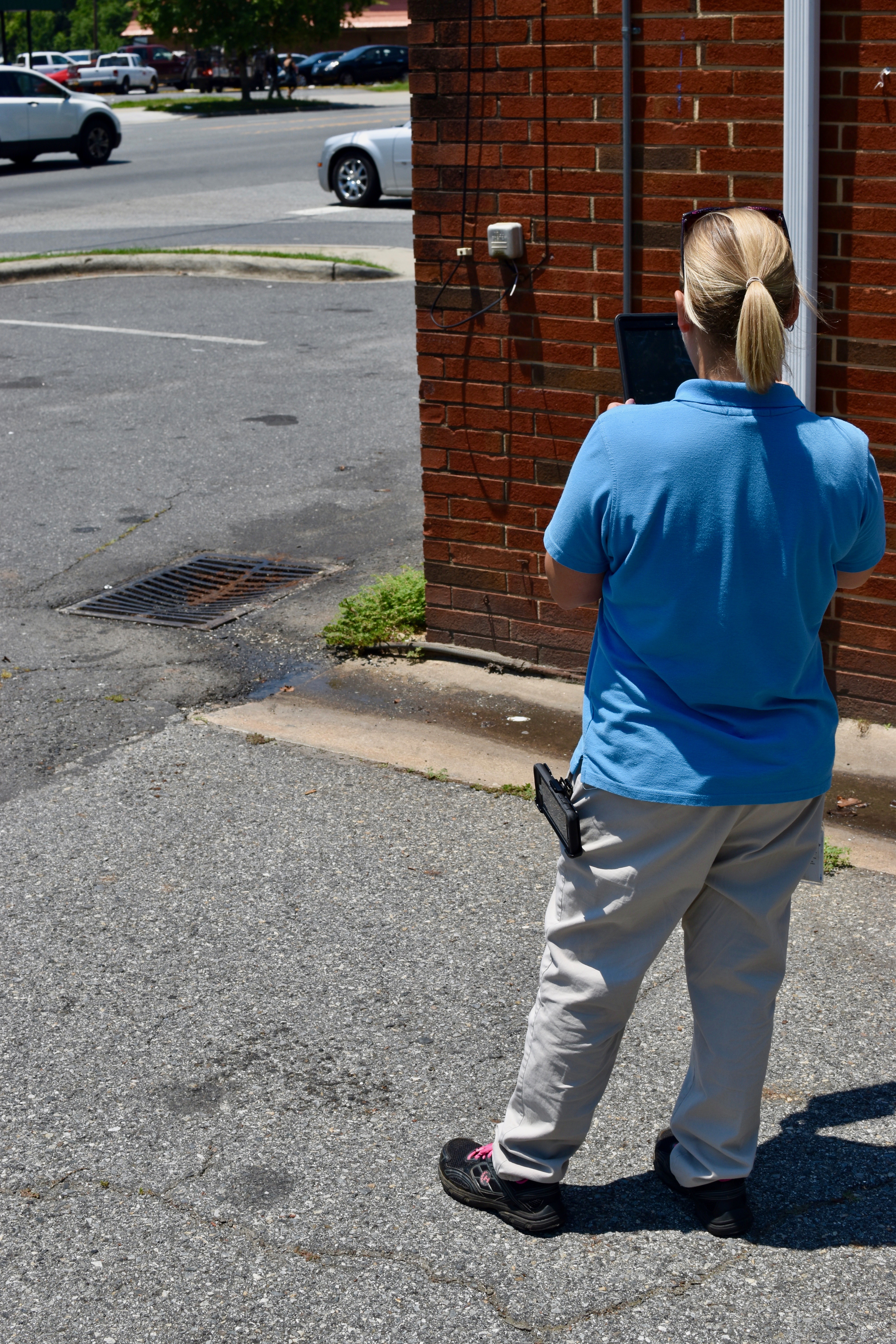 utility engineer with blonde pony tail and blue polo shirt reviews a sewer drain grate using a ipad camera