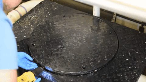 video clip of a blue gloved hand opening a black round lid to reveal waste settling in a tank