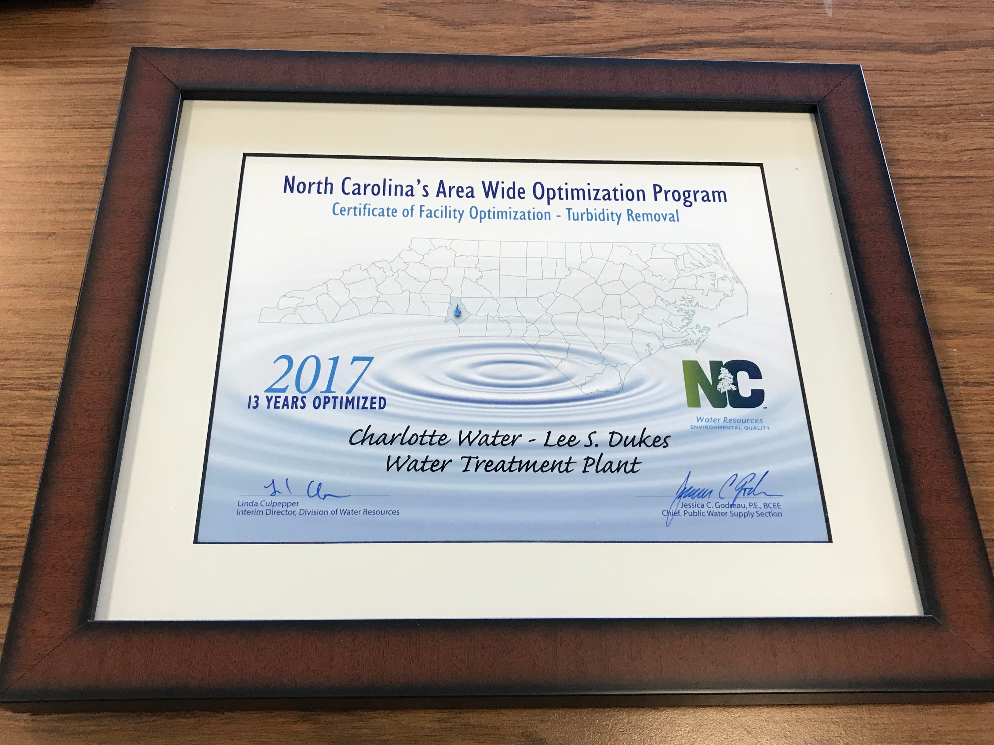 wood framed white and tan award certificate in black and blue font for Charlotte Water - Vest Water Treatment Plant on behalf of the North Carolina Area Wide Optimization Program Certification of Facility Optimization - Turbidity Removal, 2017 ten years optimized