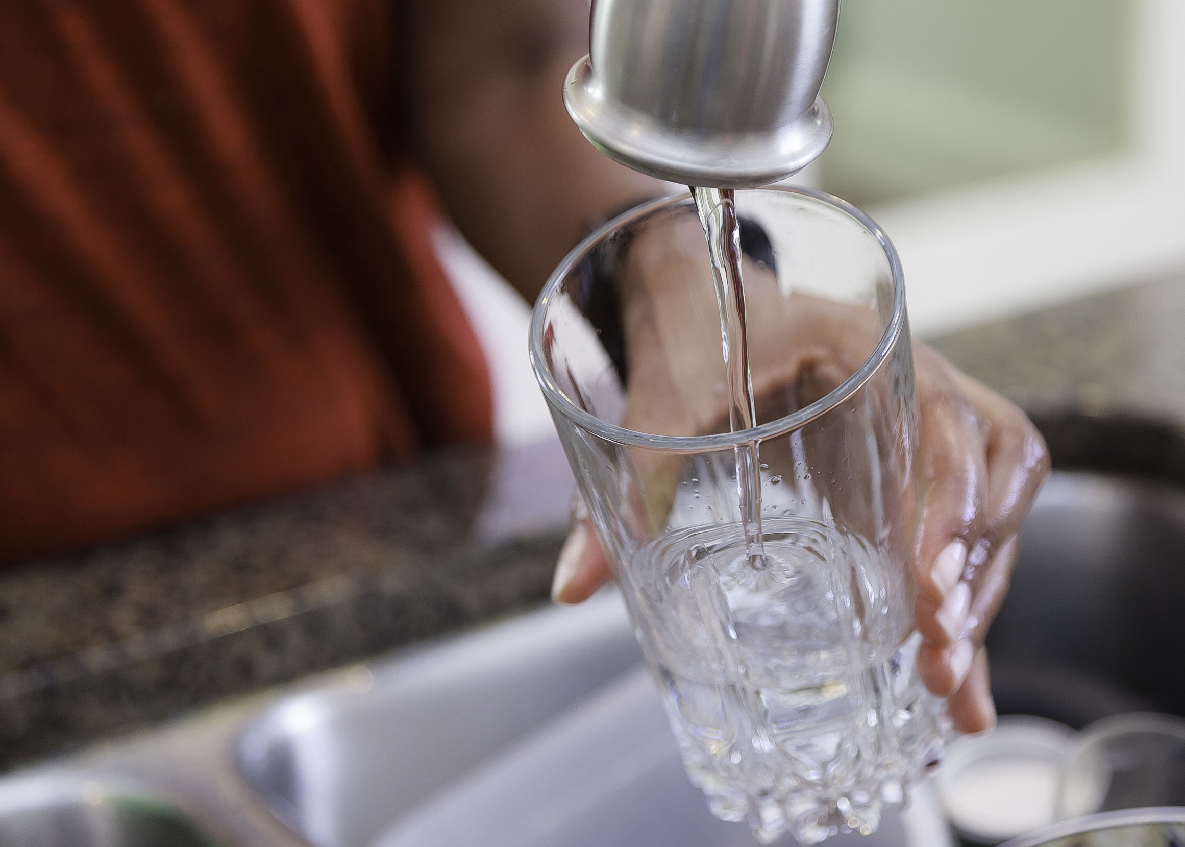 hand holds a glass filling it with water from a pewter colored faucet head