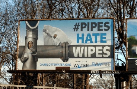 Billboard of 2 utility mascots, pipe lady and wipes man, with hashtag #pipes hate wipes in large font with Charlotte Water logos