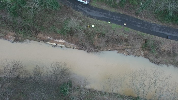 birds-eye view of a muddy stream as it passes by a paved roadway in a wooded area