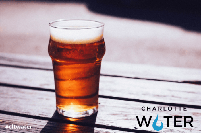 beer in a clear glass sits on a brown picnic table, in the foreground is the Charlotte Water logo