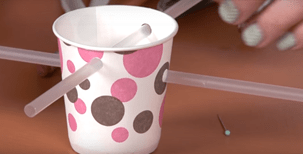 2 clear drinking straws are inserted into holes on either side of a white paper cup with brown and pick polka-dots