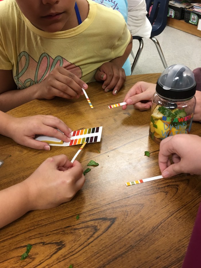 hands of children on a wooden table explore the words and colors on ph test strips