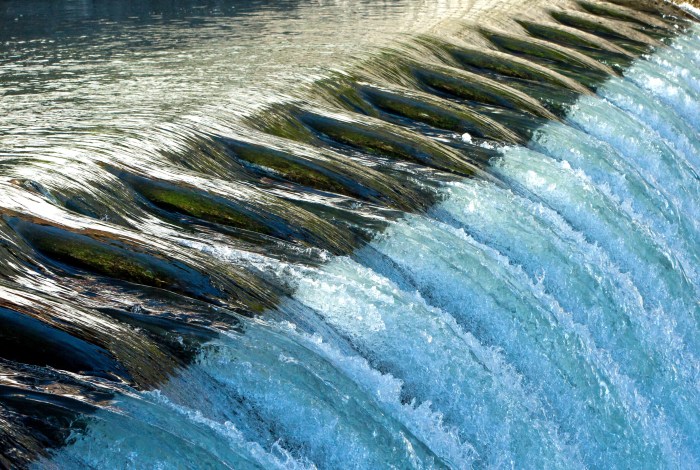 water rushes over a dam overflow creating a waterfall of splashing white water