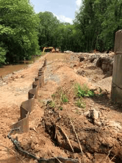 eroded earthen retention wall and washed out piles of mud sits next to muddy pond