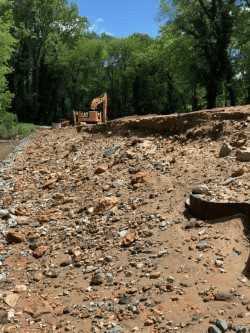line of gravel and earth in a pile, in the distance is a yellow excavator