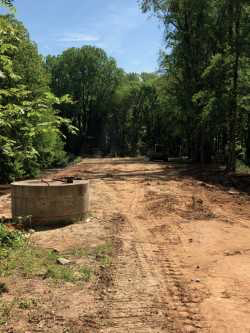 recently installed round concrete raised manhole with metal cover and metering caps sits alongside a restored recently excavated dirt road