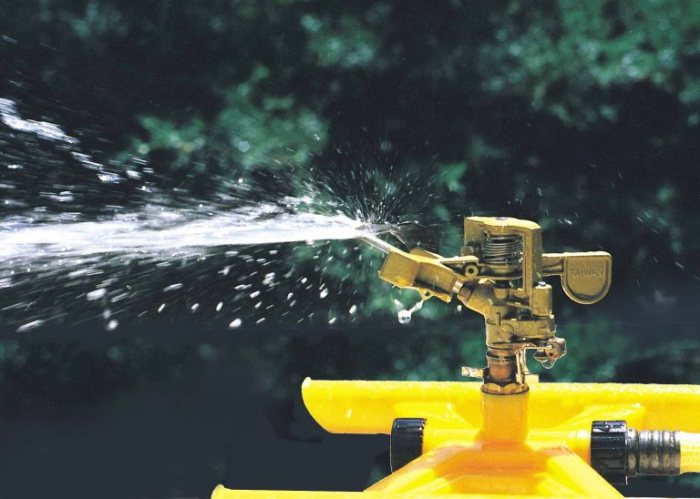 close up image of a yellow plastic lawn sprinkler with a brass head slapping water into the air