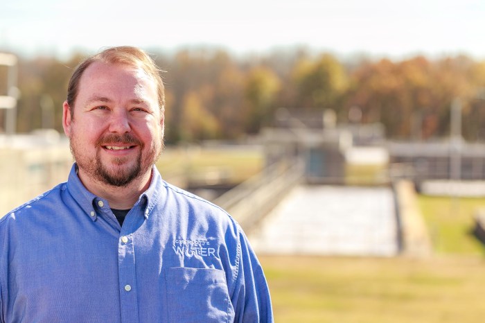utility employee wearing blue button-down shirt with Charlotte Water logo stands outside in front of rectangular pool at a water treatment facility