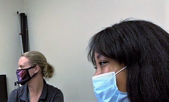 2 utility office workers wearing face masks watch something off-screen
