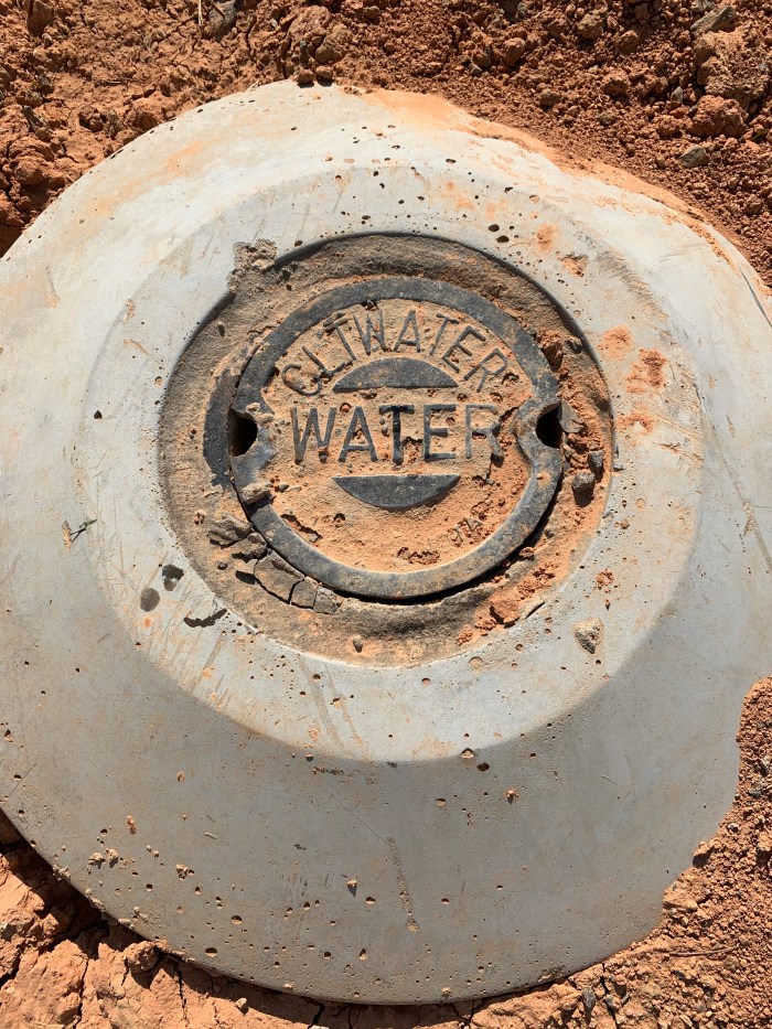 grey round concrete and metal marker newly installed in the dirt, CLTWater WATER are inscribed into the metal lid