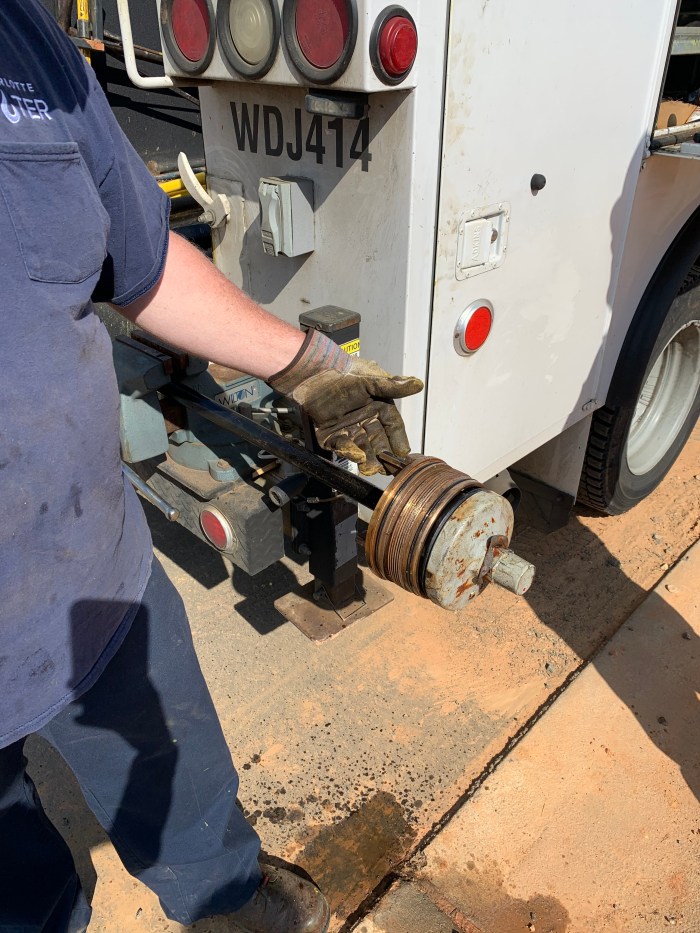 grey gloved hand of a utility technician shows off a copper cufflink part as it is poised from removal from its holder on the back of a white utility truck