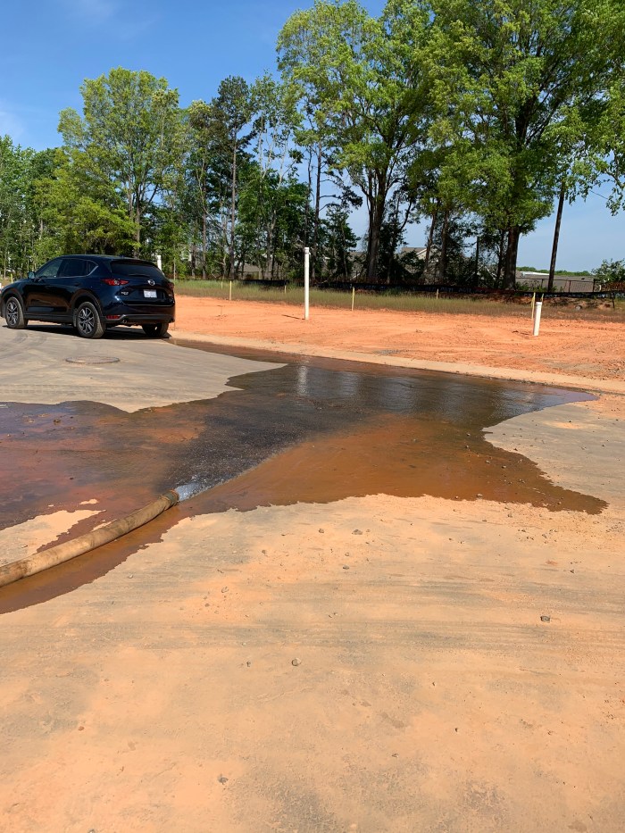 water pools and spills across a suburban, tree-lined street with a black SUV parked nearby