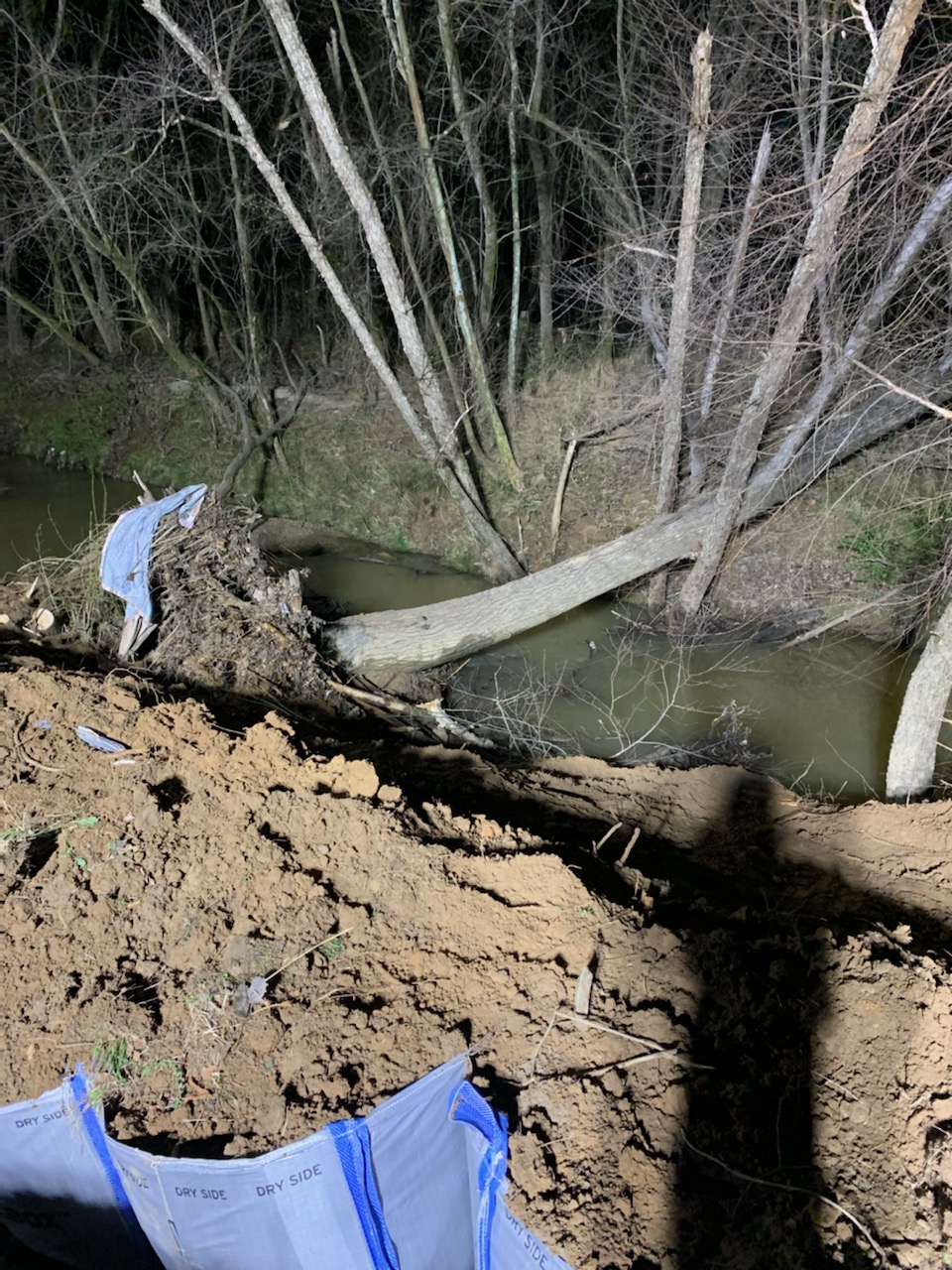nighttime view of a fallen tree over a creek near direct piles of a construction site