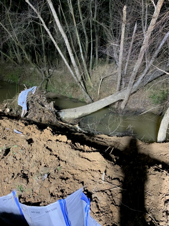 nighttime view of a fallen tree over a creek near direct piles of a construction site