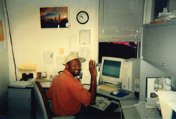 photo of utility employee wearing orange shirt and white hat and seated at his desk from approximately 20 years ago