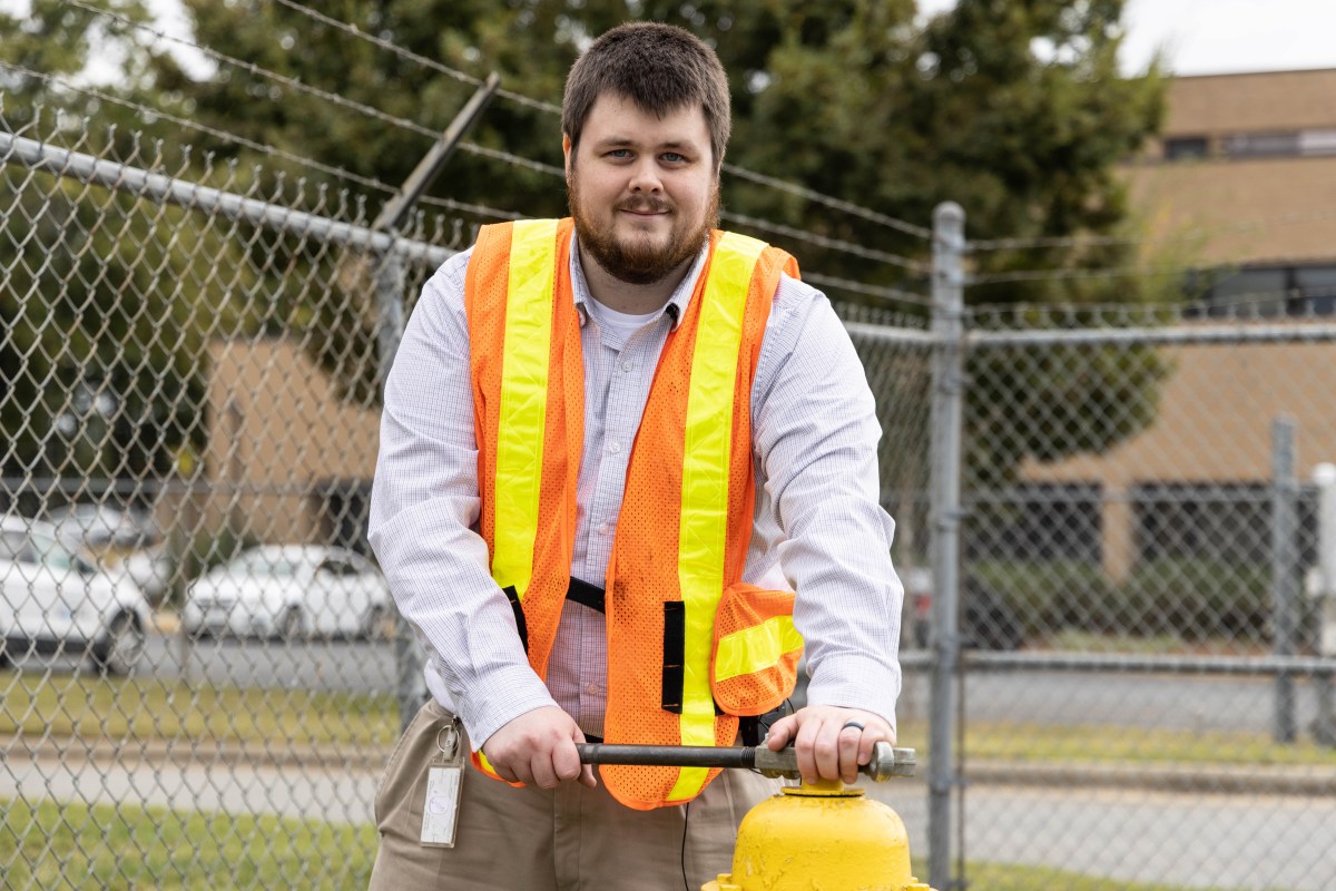 utility technician wearing orange safety vest positions a large metal wrench to open the top of a yellow fire hydrant