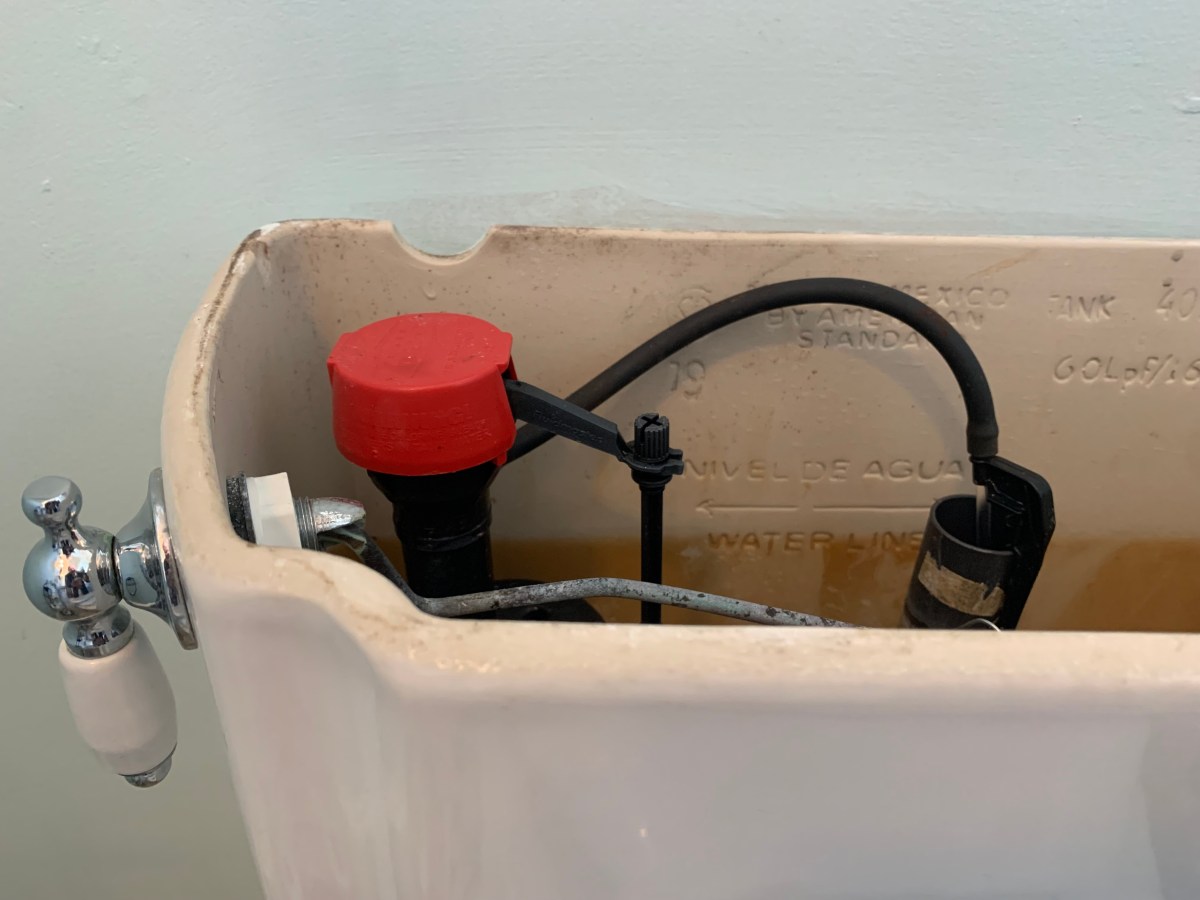open white toilet tank revealing red and black flapper mechanism