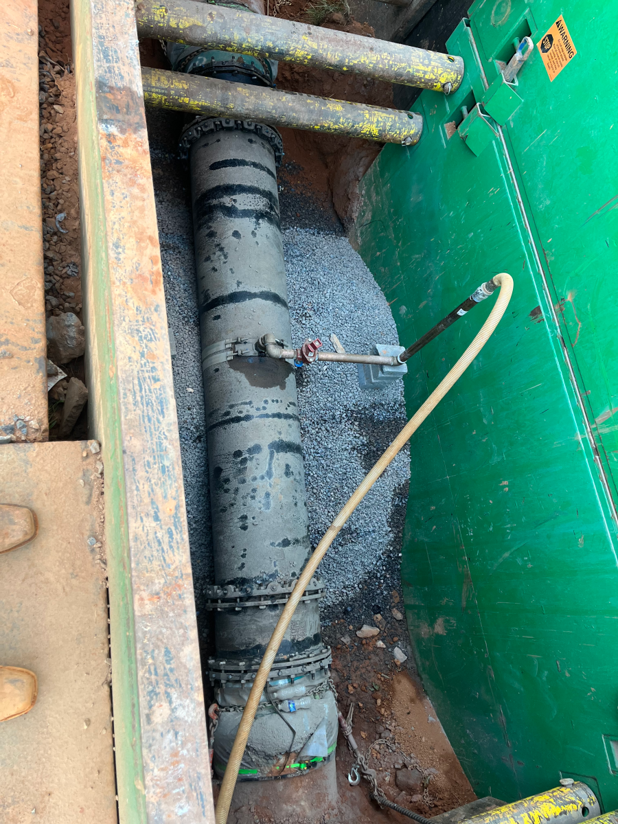 view of a large grey pipe and yellow metering cable in a subterranean, green metal chamber