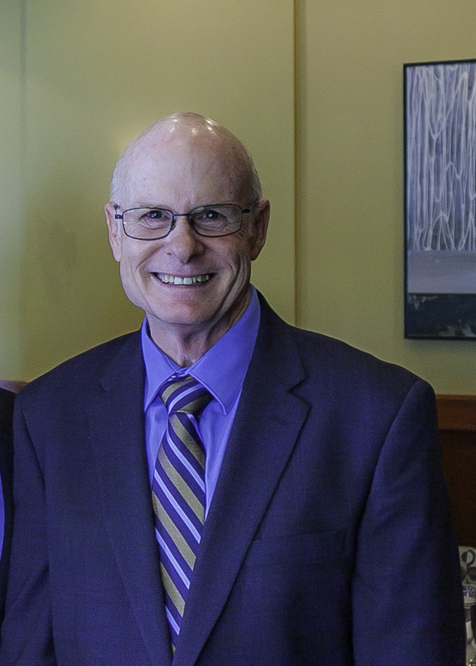 Man wearing blue suit, blue dress shirt and gold with blue striped necktie and glasses poses for a photo in a restaurant