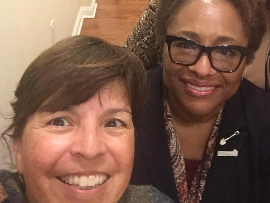Two female utility staff members take a selfie, one wears a pin on her label of a shovel