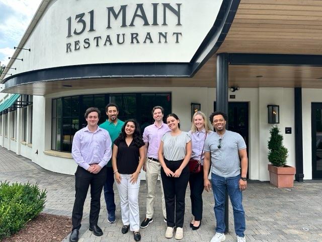 7 student interns pose for a photo outside in front of a sign 131 Main Restaurant