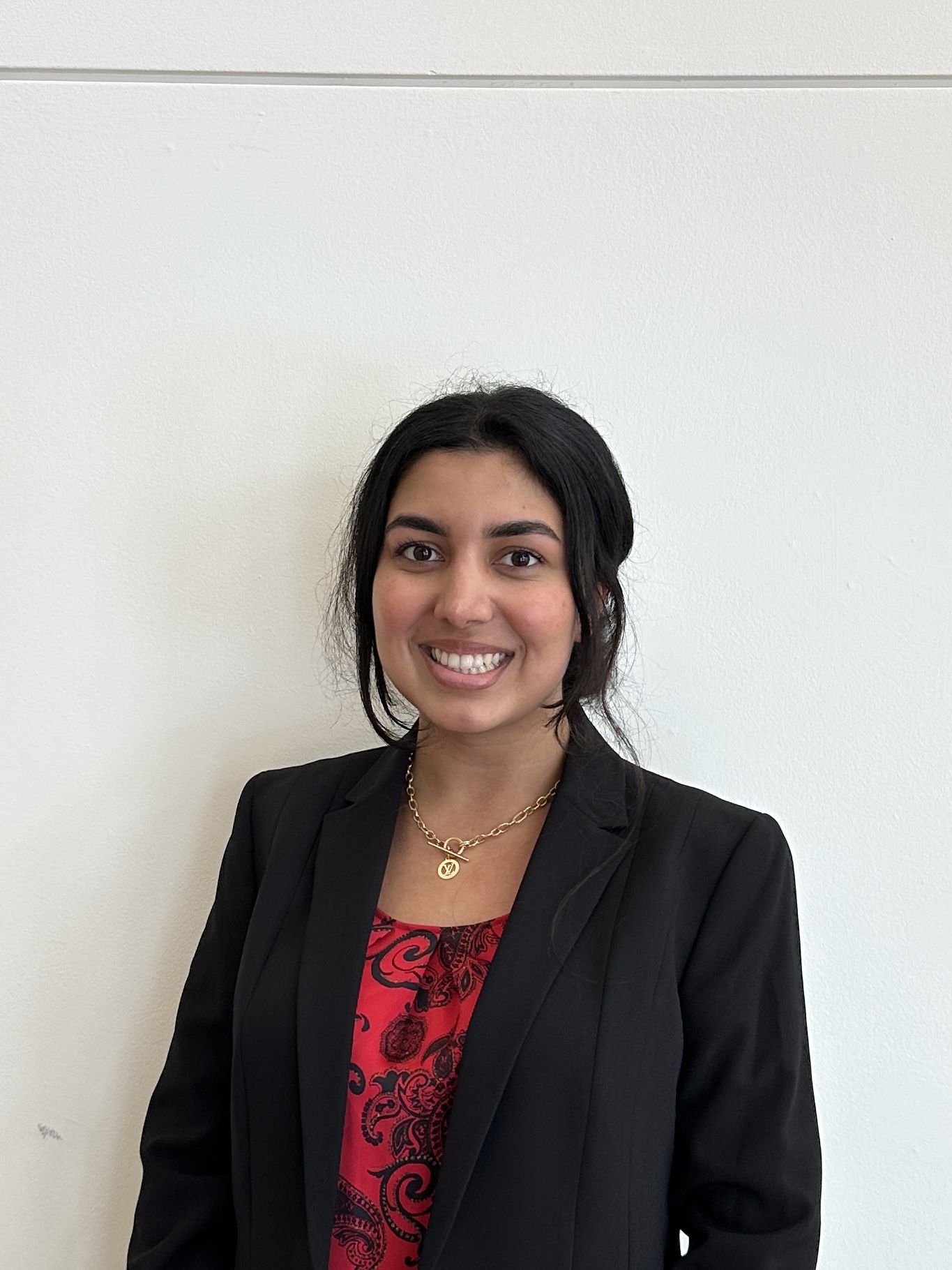 Profile photo of utility intern with dark hair, wearing a gold necklace, black jacket and red and black patterned blouse