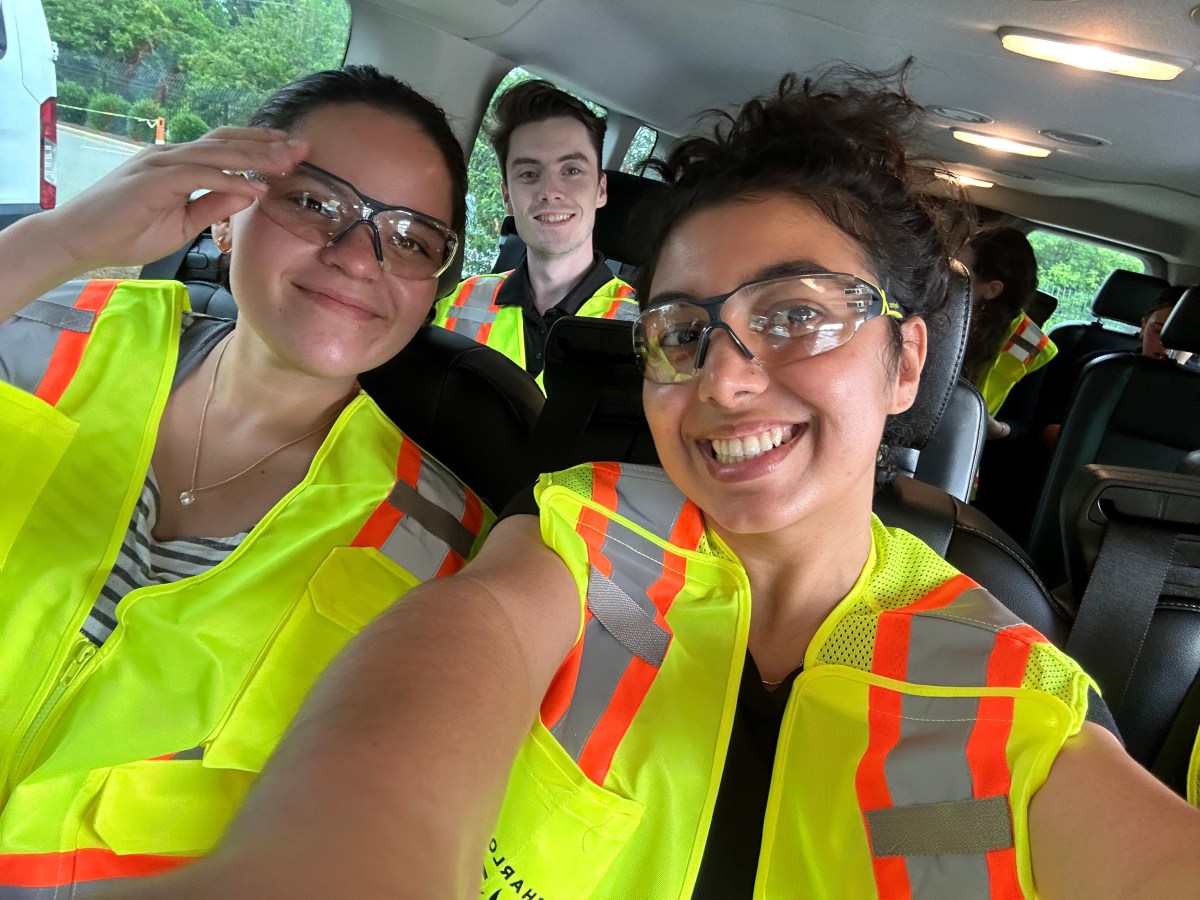 Selfie photo of 3 student interns wearing yellow safety vests seated in a van