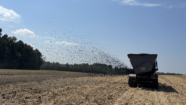 An agricultural manure spreader truck sprays biosolids into the air to fertilize acres of empty, brown farmland