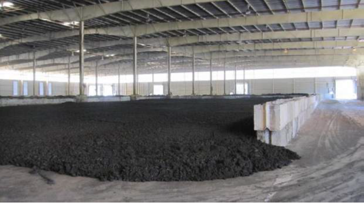 Large pile of charcoal-colored biosolids sitting on a expansive concrete floor in a very-large warehouse storage space