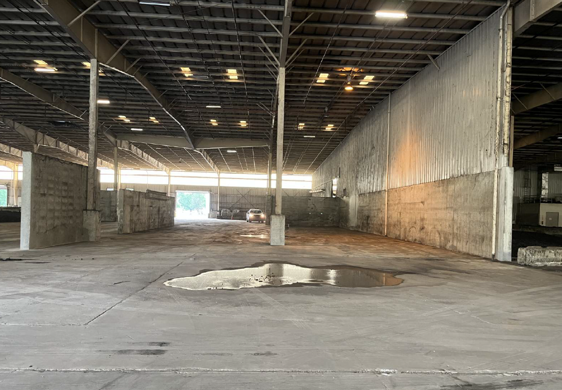 Large, tall, empty storage warehouse with grey painted walls, expansive concrete floors and a large puddle of water