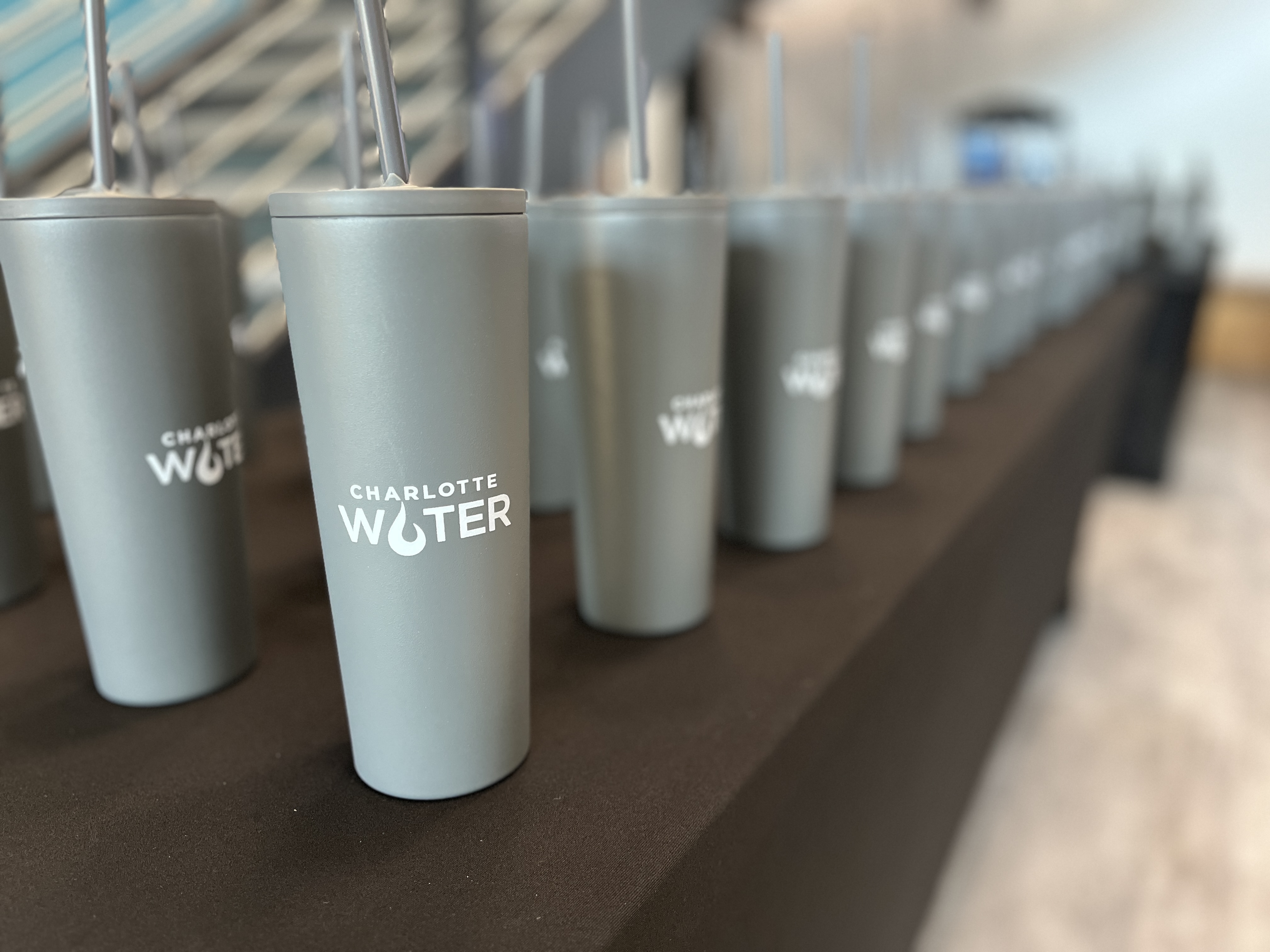 Dozens of grey Charlotte Water branded cups with straws sit on a table