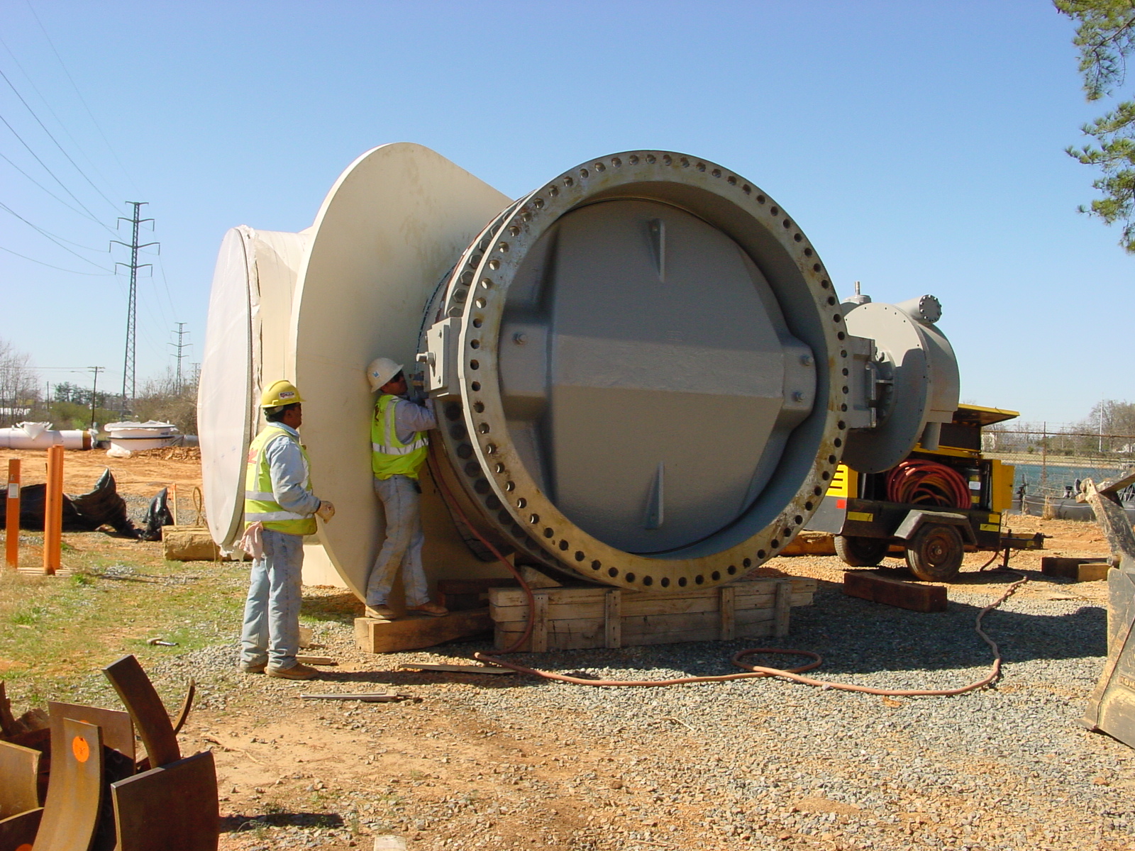 2 utility crewmen wearing yellow safety vests and hard hats preparing to install a very large concrete transmission water main valve