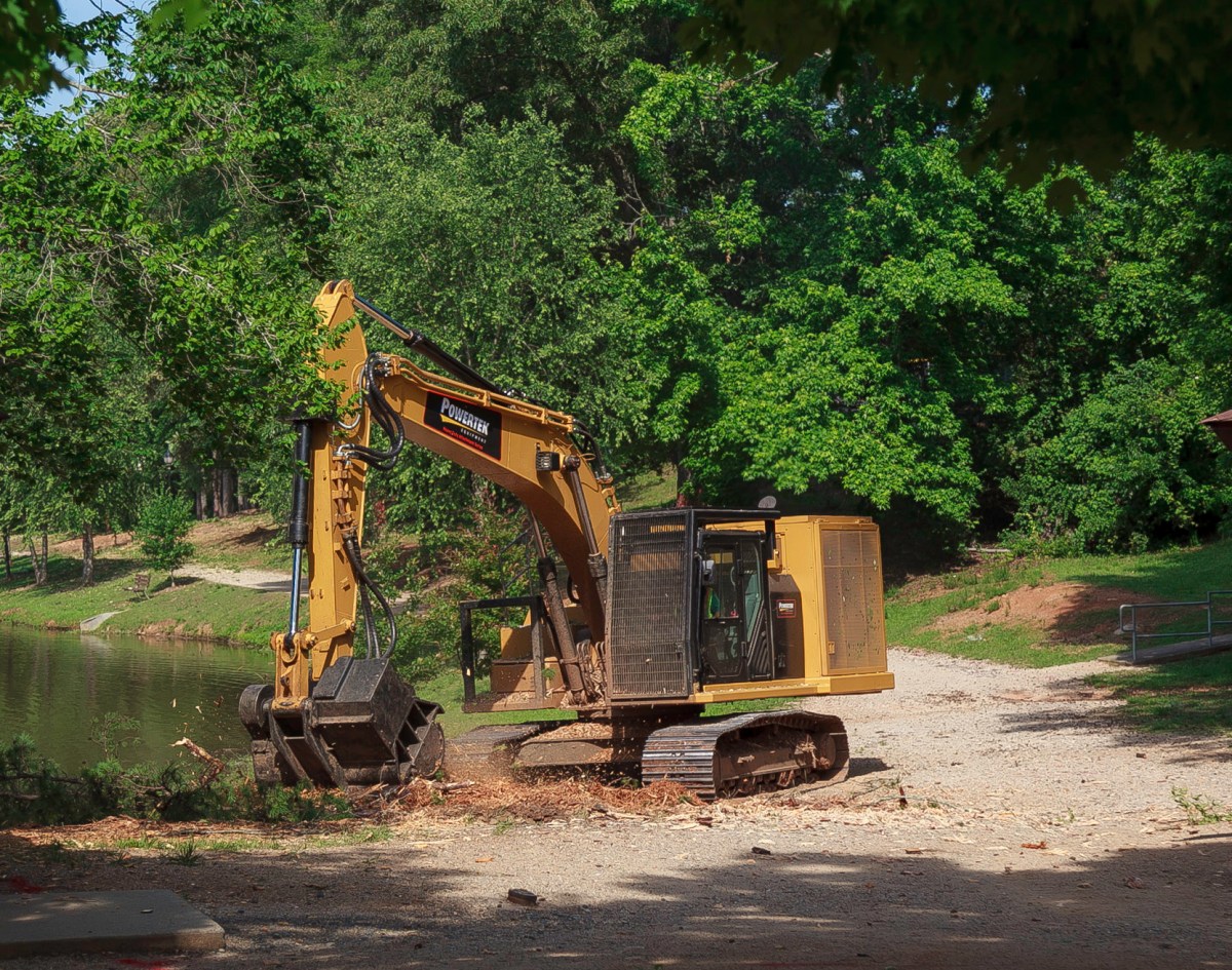 Yellow excavator with a stump grinder attachment chews up a large tree stump