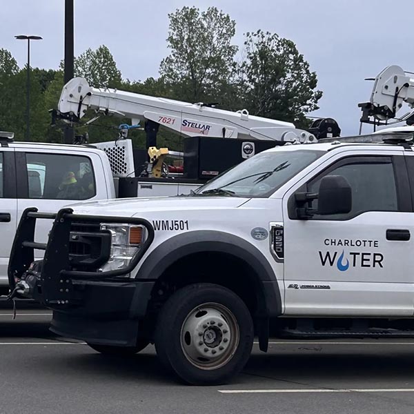 2 white utility pick up trucks wait in parking lot to be called for emergency support, one of the trucks has a mini-crane attached to it